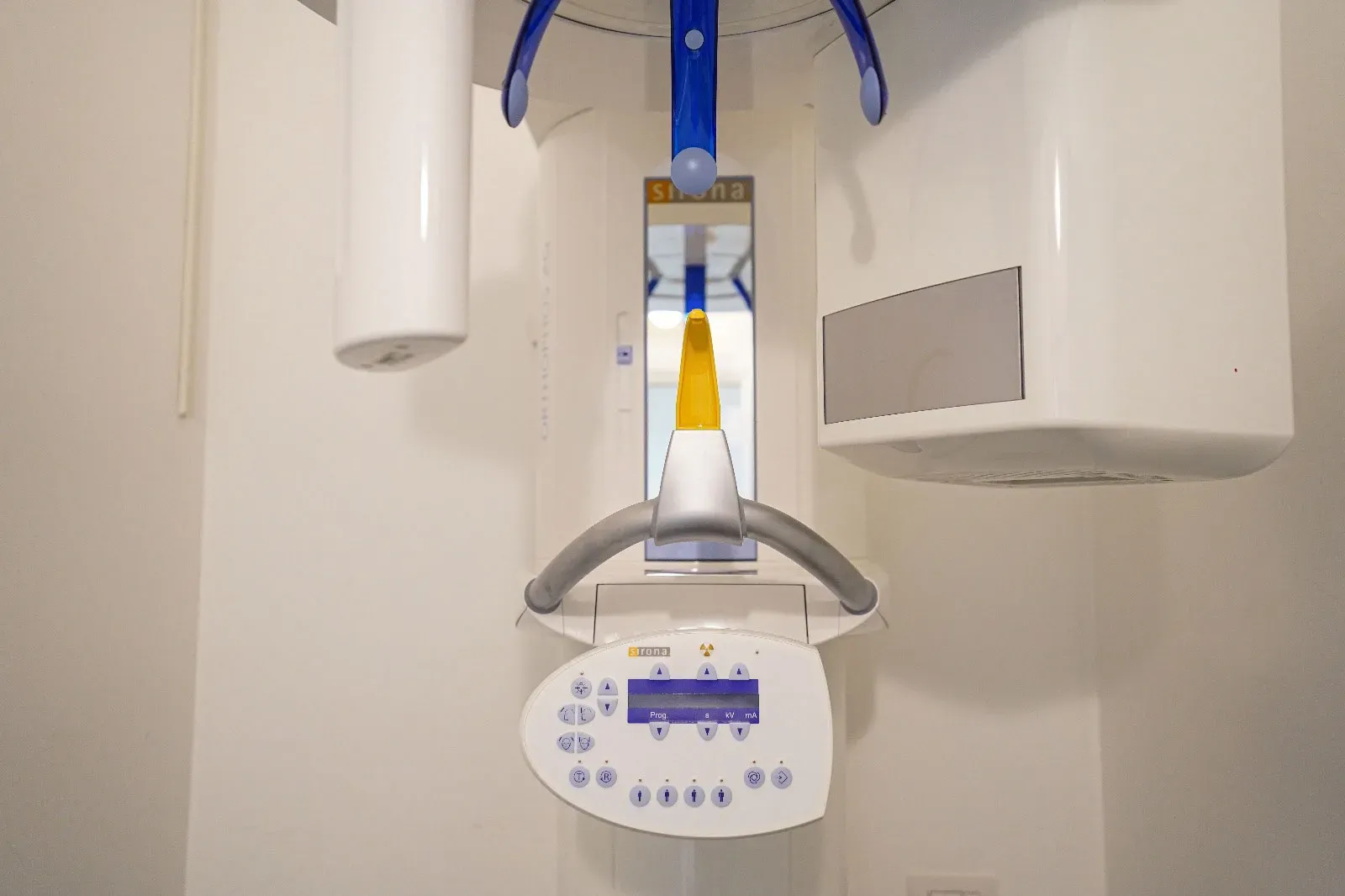 Ortopantomografo Sirona bianco con mordente giallo, appoggi blu per la testa e pannello comandi Prog kV mA